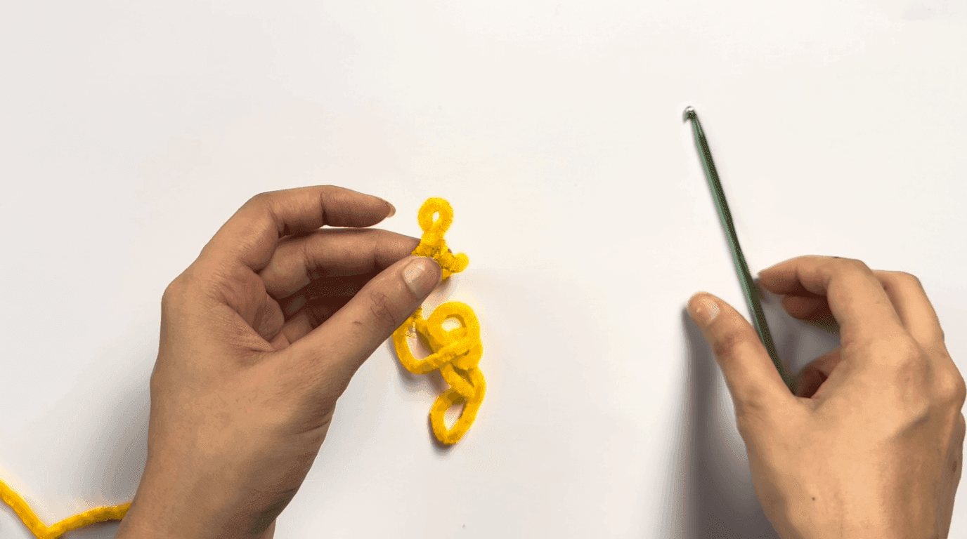 Hands demonstrating how to create a chain start for the crochet duck pattern using yellow yarn and a 4mm hook on a white background.