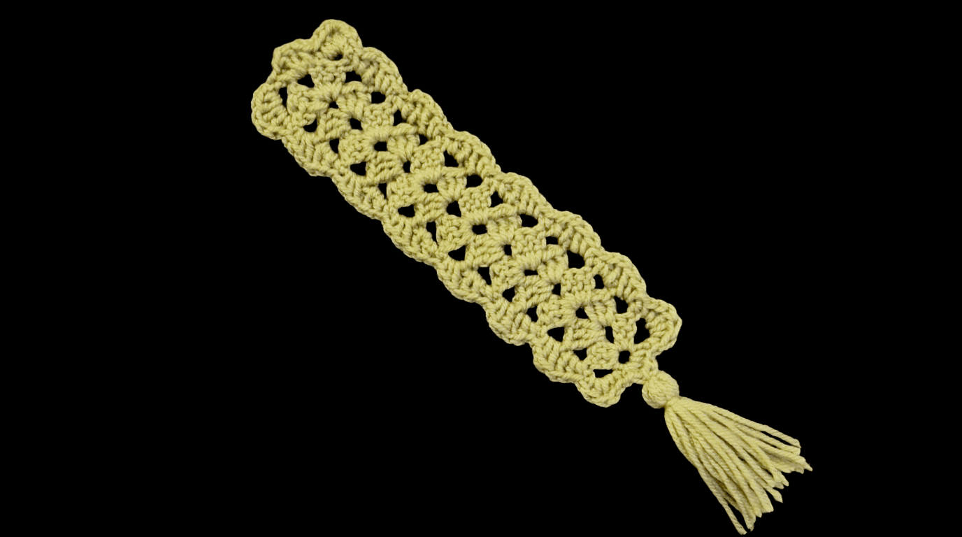 Finished granny stripe crochet bookmark with a green tassel, laid on a dark reflective surface