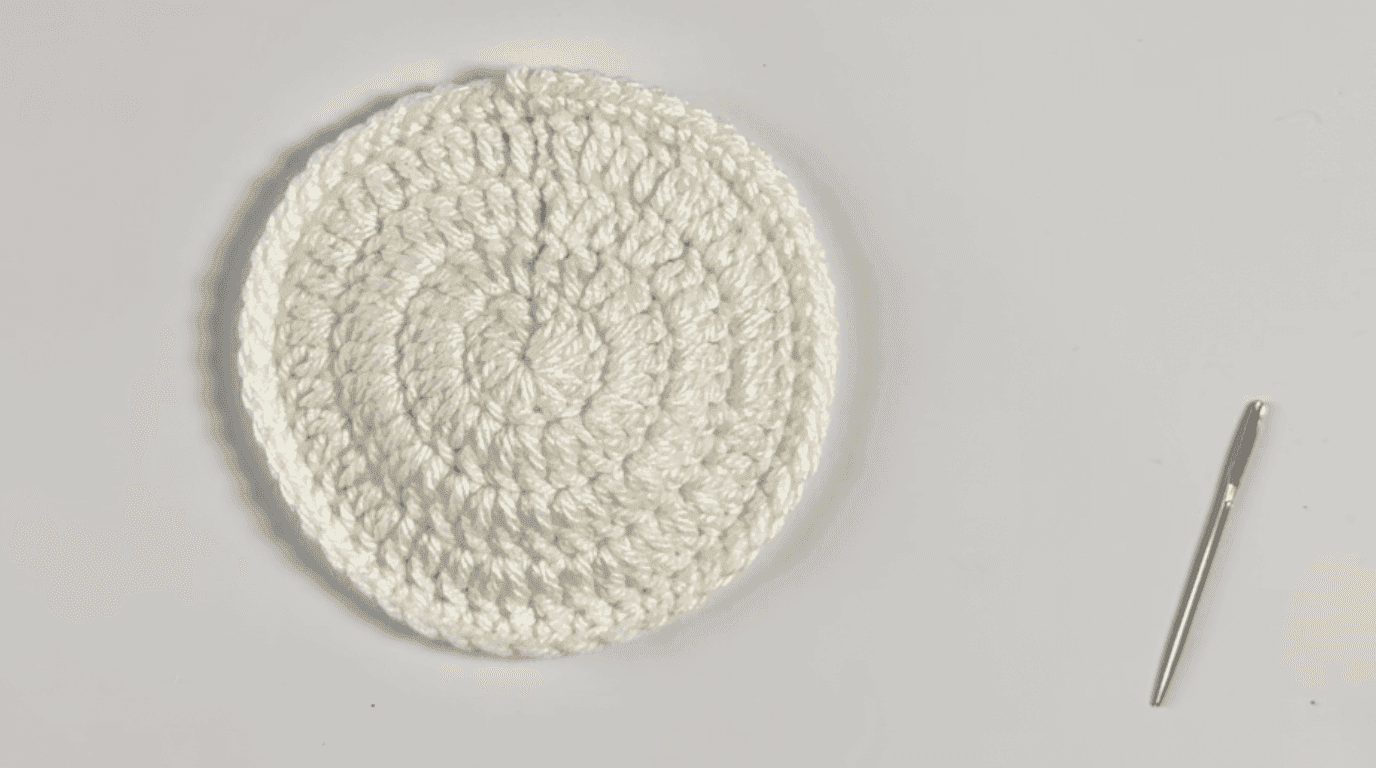 Completed crochet sunflower coaster base: finished cream-colored flat coaster with all yarn ends woven in and ready for green leaf attachment