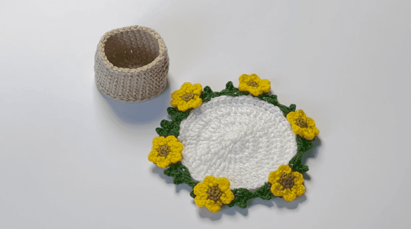 Completed crochet sunflower coaster: overhead view showing cream base with green leaf edge and yellow flowers radiating around entire piece