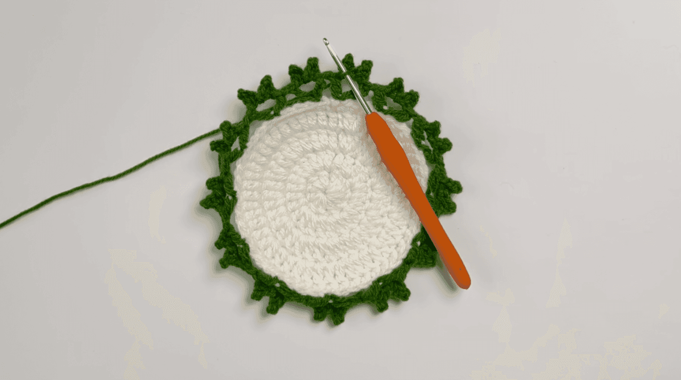 Crochet sunflower coaster leaves Round 2: coaster edge showing forest green leaf clusters radiating outward, demonstrating completed leaf pattern around partial edge
