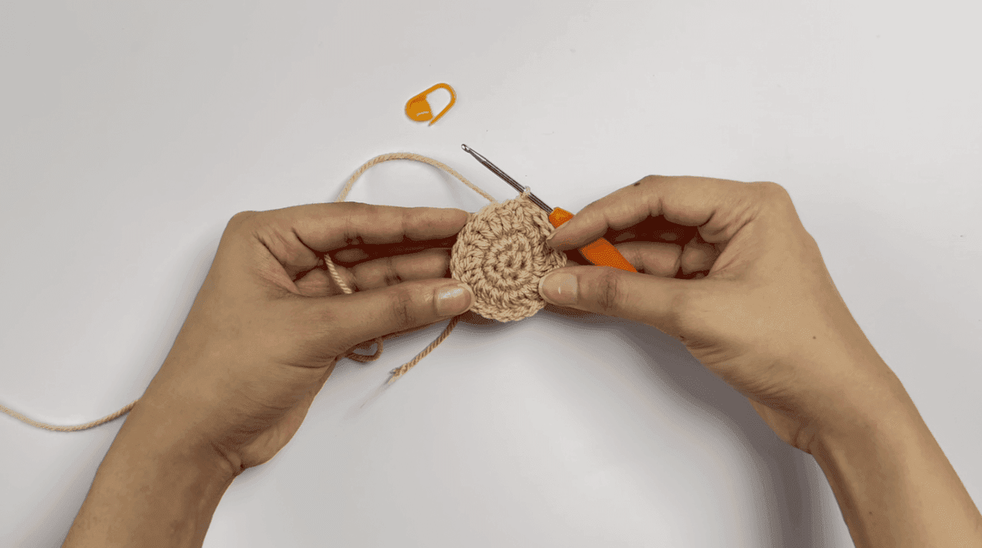 Crochet sunflower pot Round 3: hands working 1 double crochet plus increase pattern repeated around growing beige base