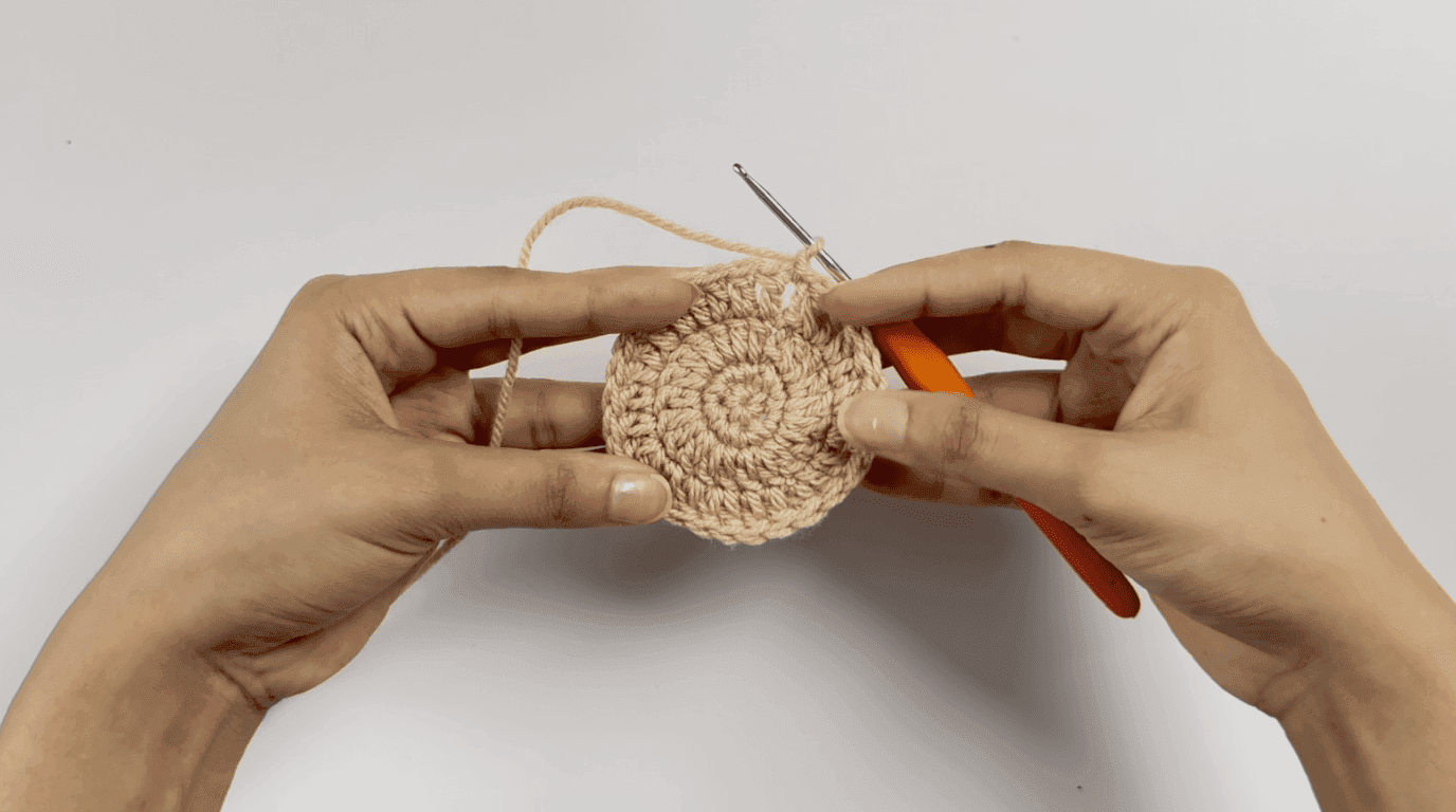 Crochet sunflower pot Round 4: hands working 2 double crochet plus increase pattern on larger beige pot base with hook