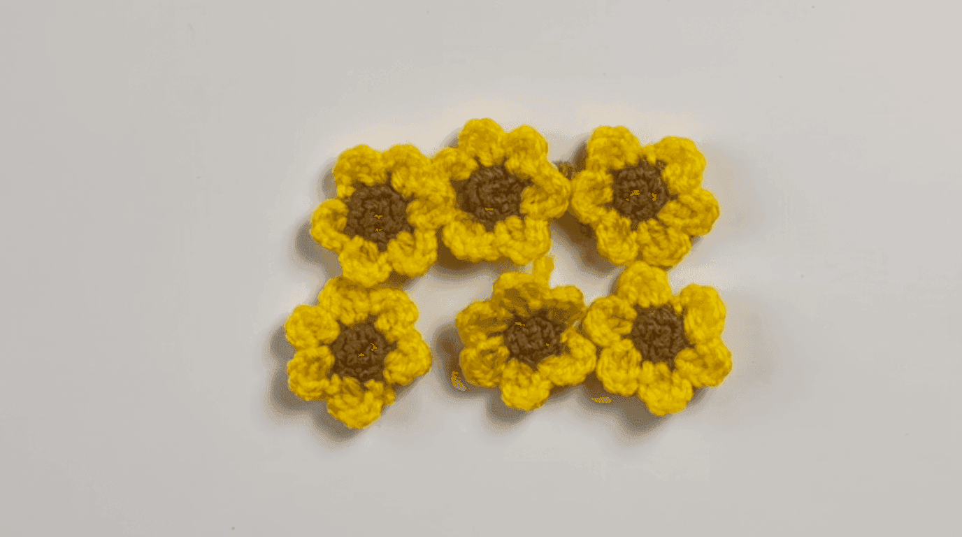 Six completed crochet mini sunflowers: brown cores with mustard yellow petals arranged on neutral background, ready for assembly