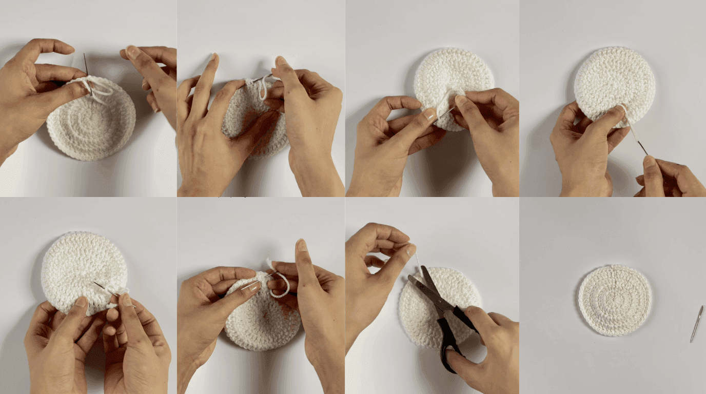 Crochet sunflower coaster finishing: hands threading yarn needle and weaving in leftover tail through back stitches to secure and hide yarn end